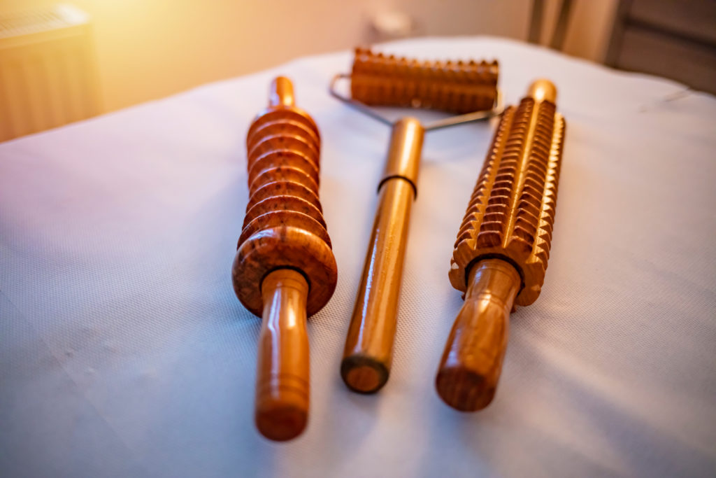 Three wooden body contouring tools arranged on a bed