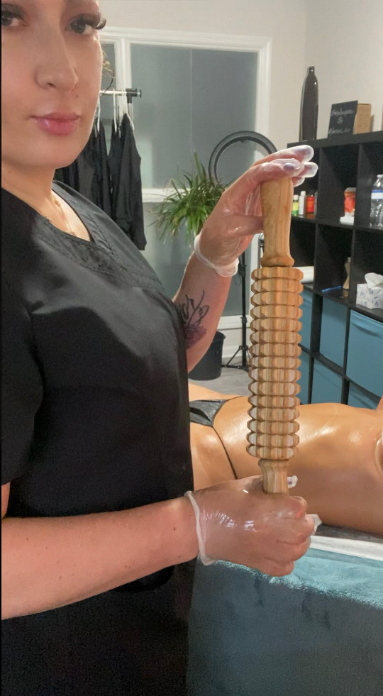Therapist in black dress holding wooden body contouring tool